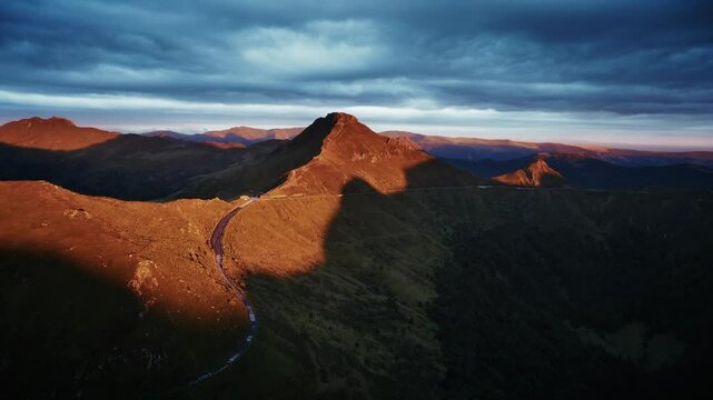 Dramatic drone aerial view of an ancient volcano at sunset, the sky is dark, Auvergne - Puy Mary, France