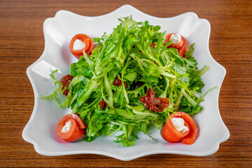 Fresh salad with arugula, salmon, cream cheese and sun-dried tomatoes on wooden table
