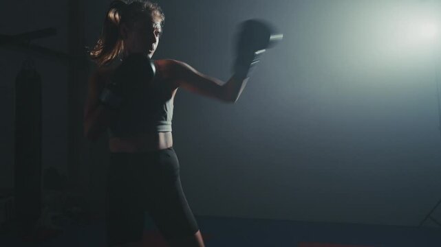 Female boxer trains intensely at night in dimly lit gym showcasing power and focus