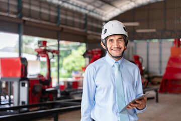 portrait old specialist manager wearing hardhat,holding digital tablet,smile,standing on site,senior male working in welding robot machine factory