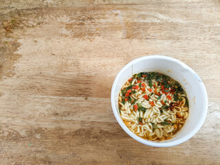 instant cup noodle with vegetables on isolated wooden background