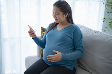 Pregnant asian woman holding smartphone at home using mobile app for pregnant women Positive life moment in pregnancy time