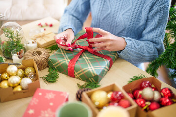 Woman in knitted sweater wrapping christmas presents with eco paper girl packing christmas gifts Xmas holiday concept