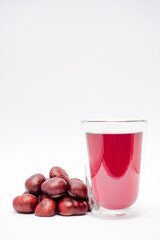 A glass of red liquid is next to a pile of chestnuts