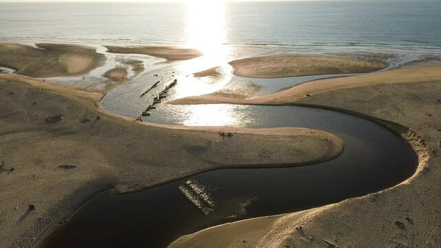 Mouth of the coastal river called Courant d'huchet in french and located on the coast of Southwestern France, in moliets commune. Aerial view during golden hour. Dolly forward.