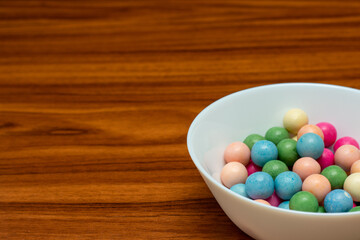 Bowl of colorful candy is sitting on a wooden table