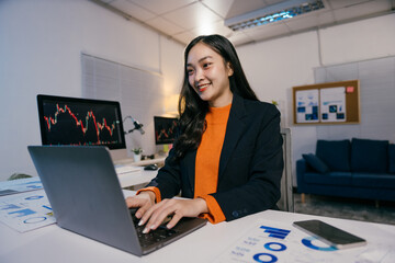 Businesswoman analyzing financial charts on laptop computer, working late to check stock market...