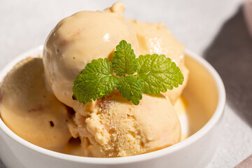 A balls of peach ice cream with a mint leaf in a beautiful creamer