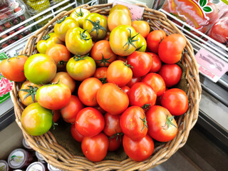 A basket of fresh, ripe tomatoes, both green and red, displayed in a market.