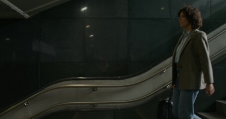A stylish woman in a jacket walks down the stairs to the subway. Dimmed lights