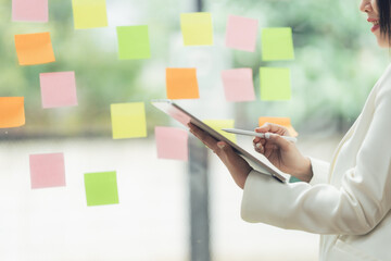 Strategizing with Technology: A businesswoman thoughtfully uses a tablet, surrounded by colorful sticky notes, reflecting a dynamic and innovative approach to problem-solving and project management.