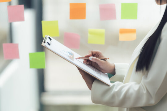 Strategic Planning Session: Businesswoman reviewing data on clipboard with colorful sticky notes background 