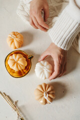 Handmade wax candle in the shape of pumpkins in the hands of a girl