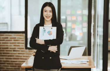 Confident Businesswoman Presenting Data:  A young Asian businesswoman smiles confidently while holding a clipboard displaying financial charts.