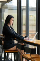 Coffee Break Productivity: A confident businesswoman smiles as she works on her laptop in a cafe,...