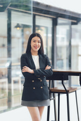 Confident and Ready: A young businesswoman stands confidently with arms crossed, exuding professionalism and determination in a contemporary business setting. Her smile suggests optimism and success.