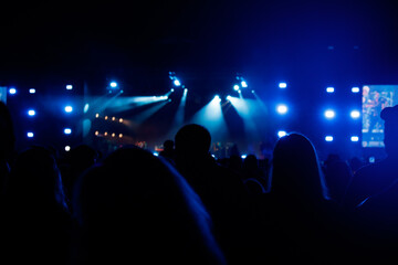 Silhouettes of spectators against a background of blue light at a concert