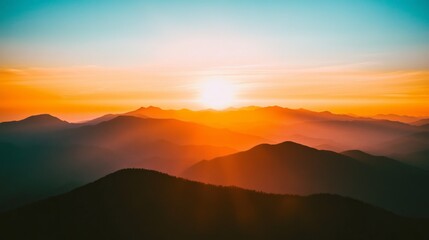 A fiery sunset over a vast mountain range with a warm glow illuminating the sky.