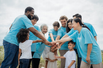 A group of people in blue shirts are holding hands in a circle. The group is made up of people of different ages. environment, clean, wind turbine, volunteer, community, teamwork, social, care, nature
