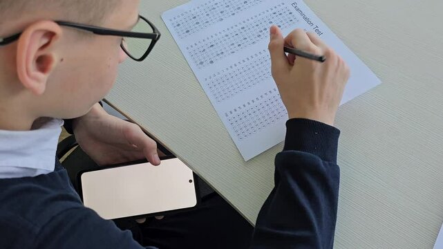 Student child holding smartphone during control exam test at school and cheating on the exam