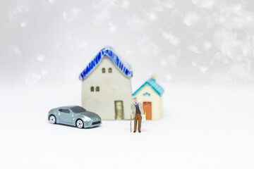 Miniature old man carry grocery bag standing with model car and miniature house with space on blurred background, insurance and retirement concept 