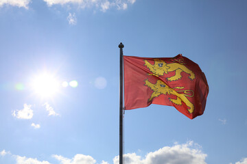 Flag of Normandy, two yellow lions on a red background, fluttering on a sunny sky.