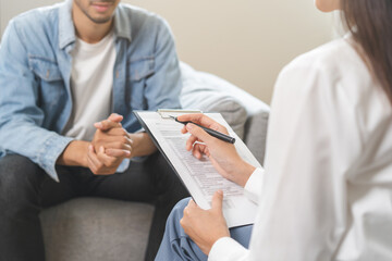 Psychology, depression. Happy smile asian young man patient mental therapy explain symptom with psychologist while doctor woman taking notes at clinic. Psychologist with sick mental health person.