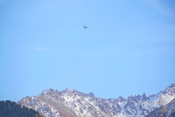 A hang glider flies over a mountainous area.