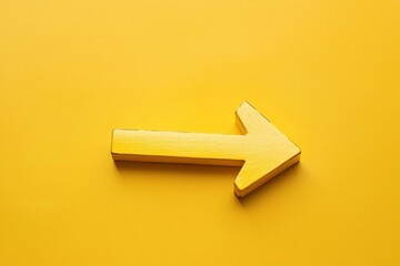 The image features a weathered yellow painted arrow positioned on a clean yellow surface, creating a contrast that highlights the arrow's texture and age against the smooth backdrop.