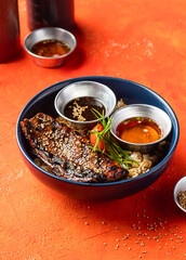 Teriyaki Grilled Bangus Belly Rice Bowl with Dipping Sauce, Green Onion and sesame seeds isolated on orange background side view of fast food meal