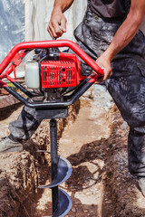 Fototapeta premium Drilling holes in the ground with a power drill. building a fence.