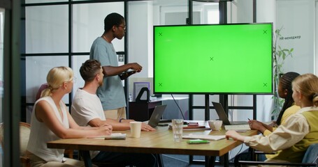 A man with a tablet in his hand is talking standing near a green screen at an office meeting. His...