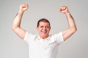 Happy older man showing off his strong biceps while standing against a light gray background