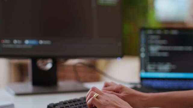 Professional software developer types code on a laptop in a sleek workspace. Asian female freelancer doing remote work on app development, software engineering and agile coding practices. Camera B.