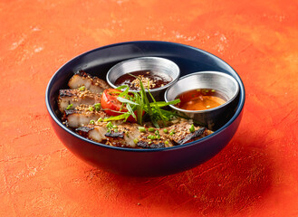 Korean Grilled Pork Belly Rice Bowl with dipping sauce isolated on orange background side view of fast food meal