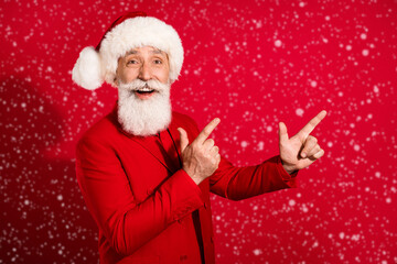 Photo of charming cute mature man dressed christmas costume hat pointing fingers empty space isolated red color background