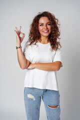 Cheerful young woman in a white shirt and ripped jeans making an okay gesture