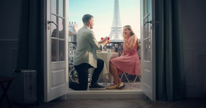 Young Handsome Man Proposing to His Beautiful Girlfriend During a Lunch on a Balcony in Paris. Eiffel Tower Standing Tall in the Background. Her Overwhelmed Reaction Captures the Magic of the Moment