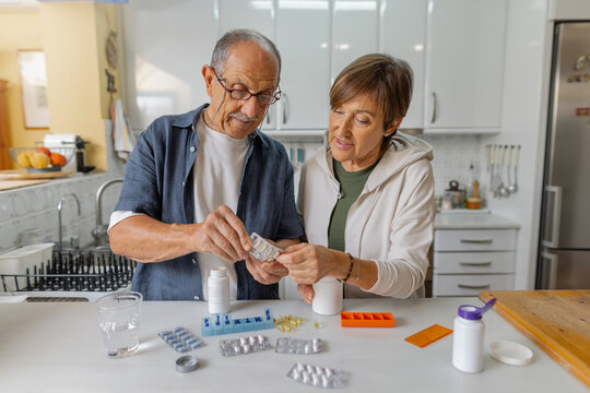 A senior couple is happily sorting and organizing their many medications together in a bright, welcoming kitchen. Elderly man and woman with casual clothes in the comfort of their home. Horizontal - Powered by Adobe