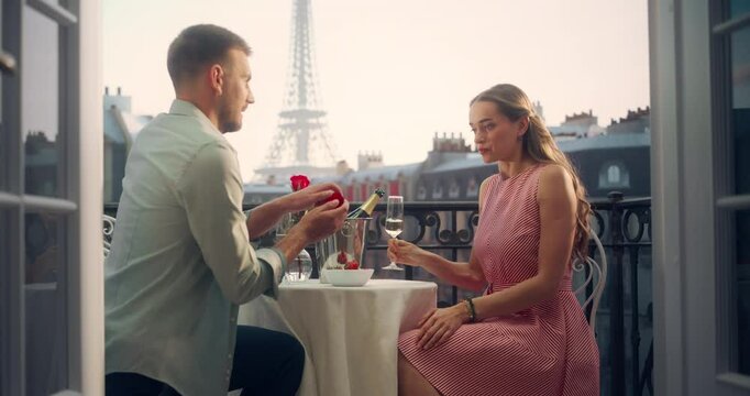 Portrait of a Young Caucasian Man Proposing to His Girlfriend with a Ring on a Parisian Balcony, With the Eiffel Tower as a Backdrop. Her Surprise and Joy Create a Romantic and Unforgettable Moment.