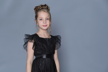 A young model in a black ruffled dress poses gracefully with her hands near her face, creating a...