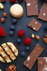 Macarons, chocolate, cookies, berries and various nuts on dark blue background. Top view.