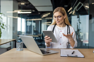 Mature woman doctor uses tablet for video consultation in office. Stethoscope around neck, she interacts confidently, illustrating telemedicine concept with laptop and documents