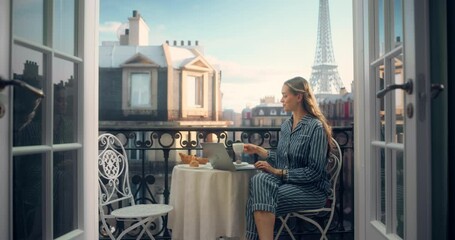 Relaxing on a Balcony in Her Pajamas, a Woman Scrolls Through News Articles on Her Laptop while Sipping Coffee. Calm of the Early Morning and Eiffel Tower View Completes Her Peaceful Start to the Day - Powered by Adobe