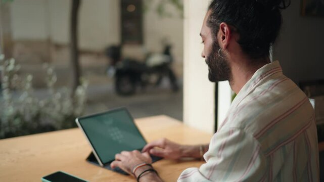 Side view of young man attempting to remember his password on tablet device in cozy cafe. Male focused expression and casual attire, relatable moment of digital security challenges. Digital nomad
