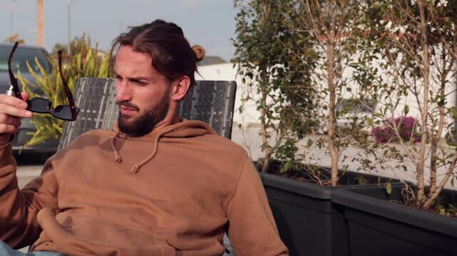 young charming and trendy guy in casual dress, relaxing on deckchair sunbathing in garden and wearing sunglasses