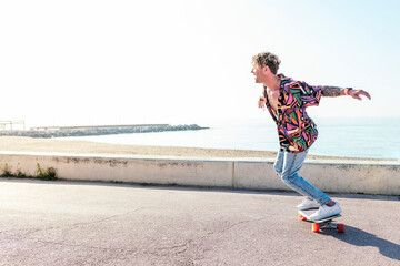 stylish male hipster in trendy wear riding modern skateboard with outstretched arms while balancing...