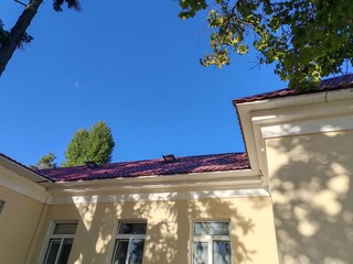 A traditional building with red accents and a tall, sloped roof, framed by trees on a sunny day....