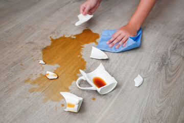 A broken cup of coffee fell on laminate, coffee spilled on floor.