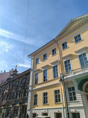 A three-story building with a pale yellow exterior and symmetrical windows, featuring a prominent arched entrance. The classical design evokes a sense of history and grandeur in urban architecture.